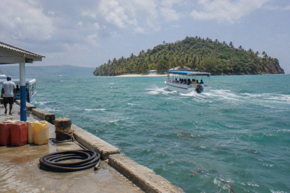 A small passenger boat crossing calm turquoise water toward a palm covered island