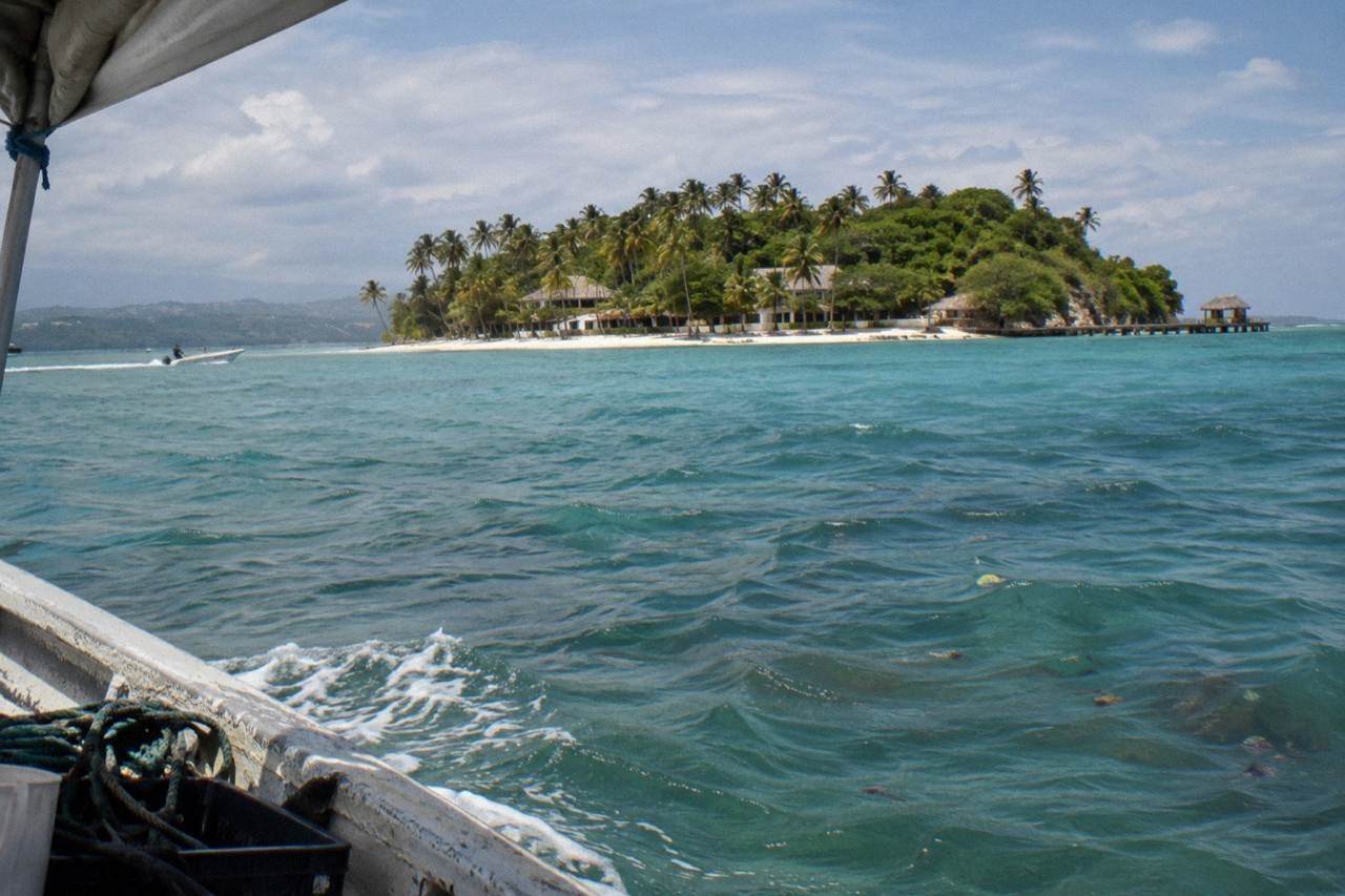 A small palm covered island with white sand rising from calm turquoise water in Samana Bay