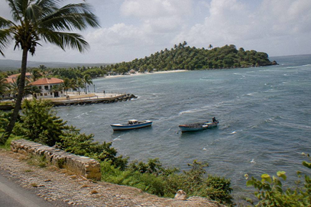 Coastal road winding along green hills above a calm bay with fishing boats