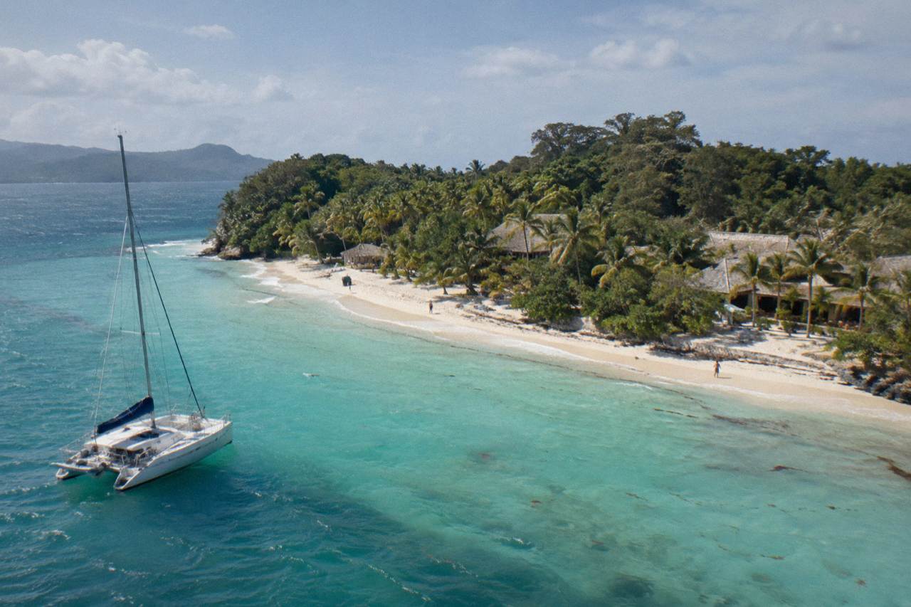 Small wooded island with a white sand beach in calm turquoise bay water under a clear sky