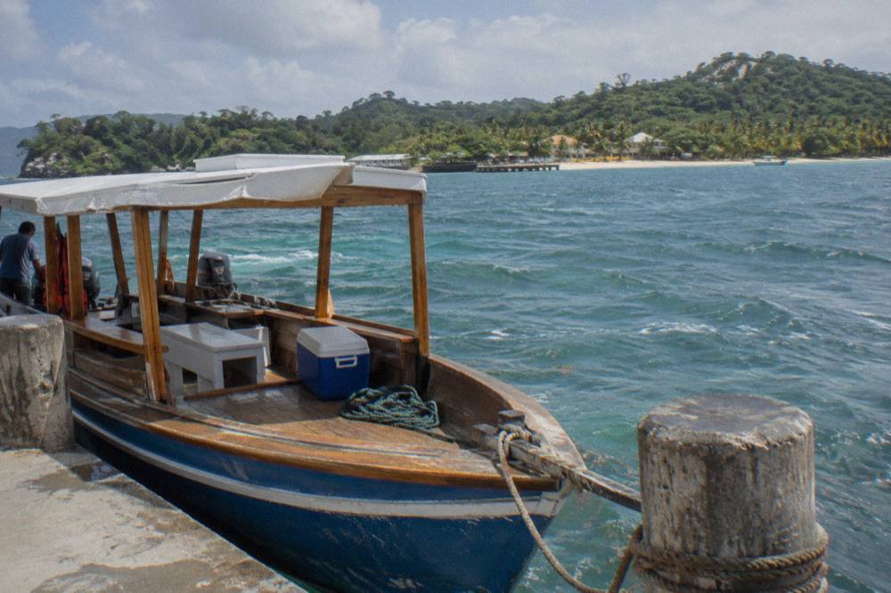 A wooden tour boat moored at a dock with green hills across the bay behind it