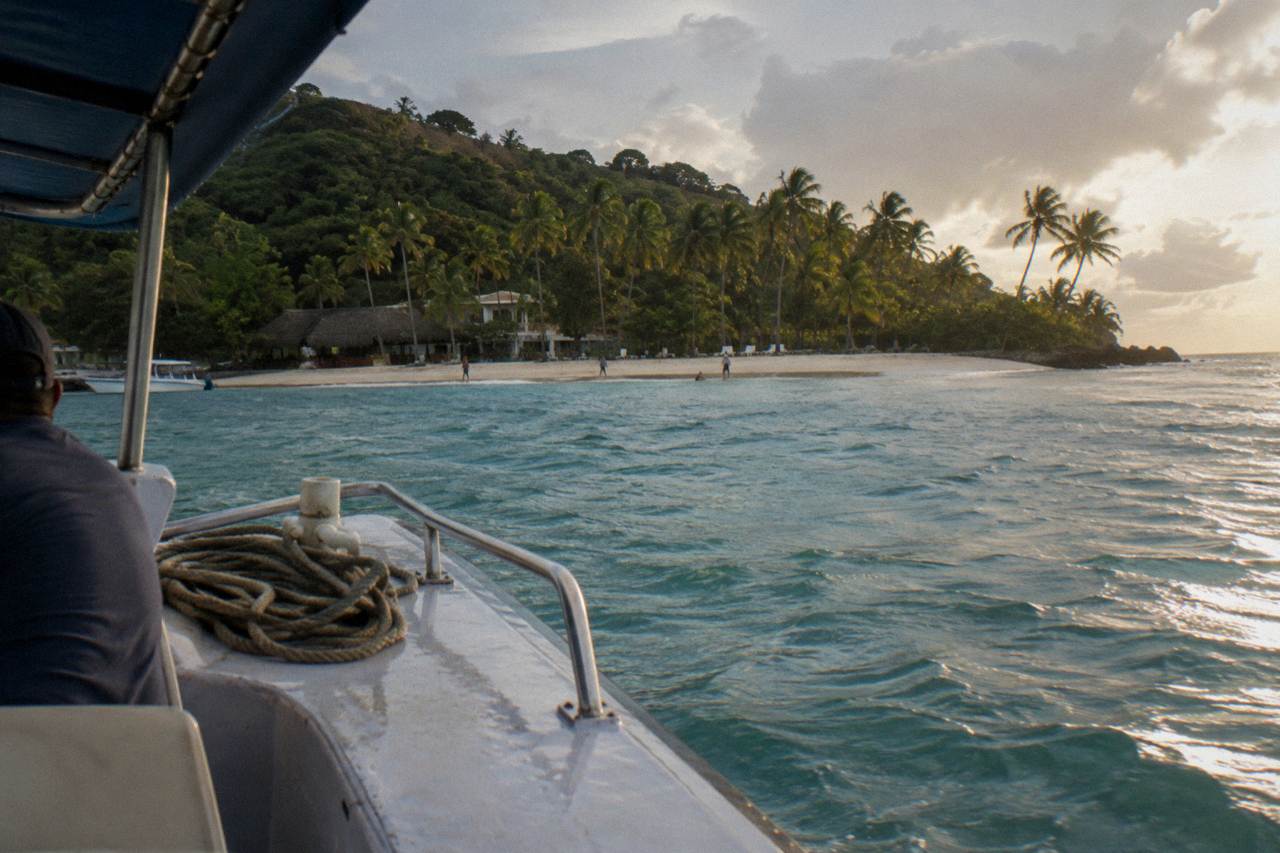 A small passenger boat approaching a palm covered island across calm turquoise bay water