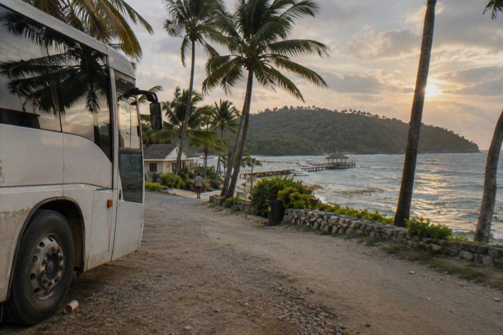 Tour bus on a coastal highway winding through green hills toward Samana Bay