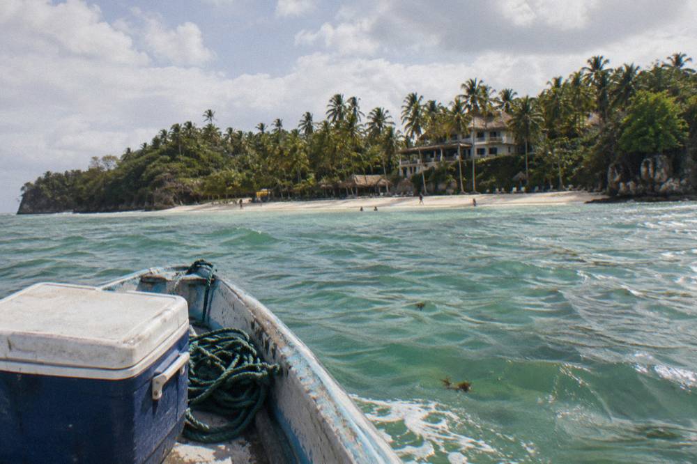 Wooden boat approaching a palm-fringed island beach across calm green water