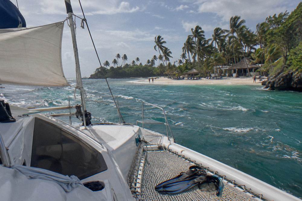 Catamaran anchored off a white sand beach with sunloungers under palms