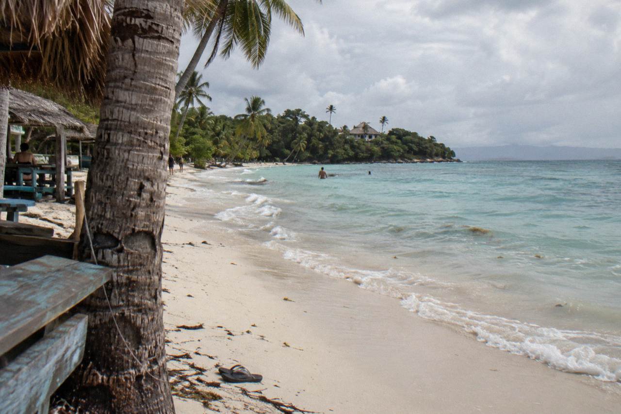 White sand beach with calm turquoise water and palm trees on a small island in Samana Bay