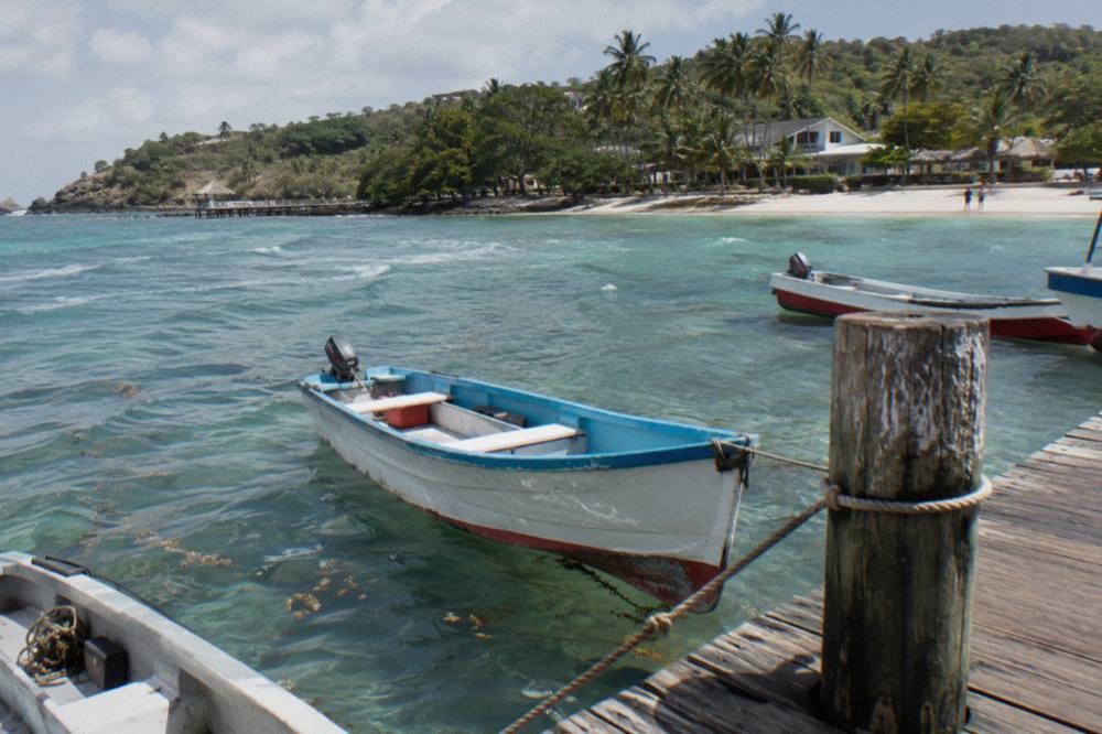 Small boats moored at a wooden dock beside calm turquoise water in a Caribbean bay