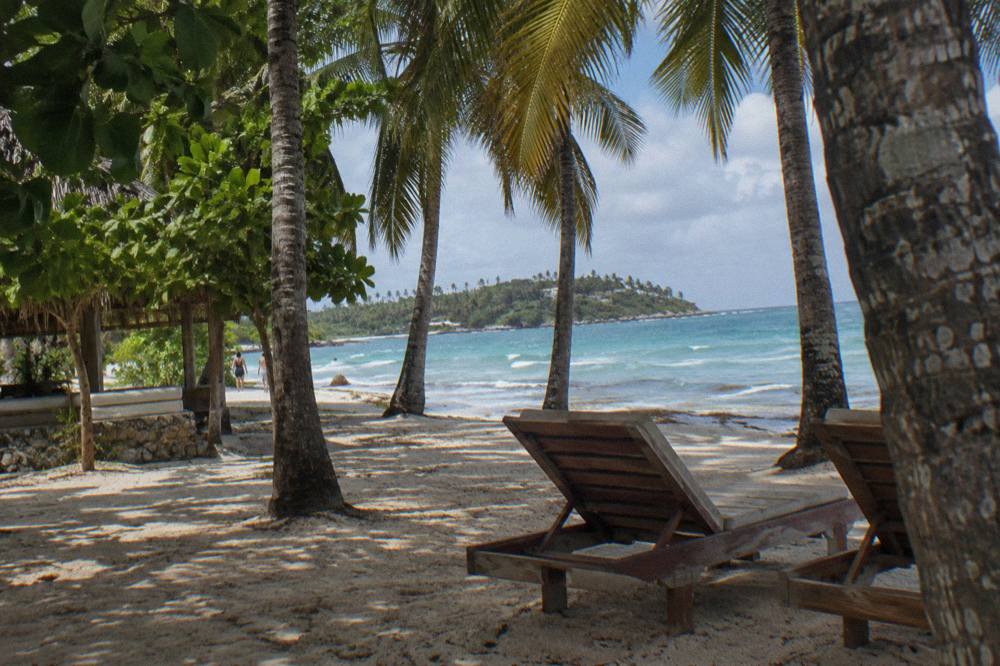 A wooden boat anchored in shallow clear water near a tree-lined shore