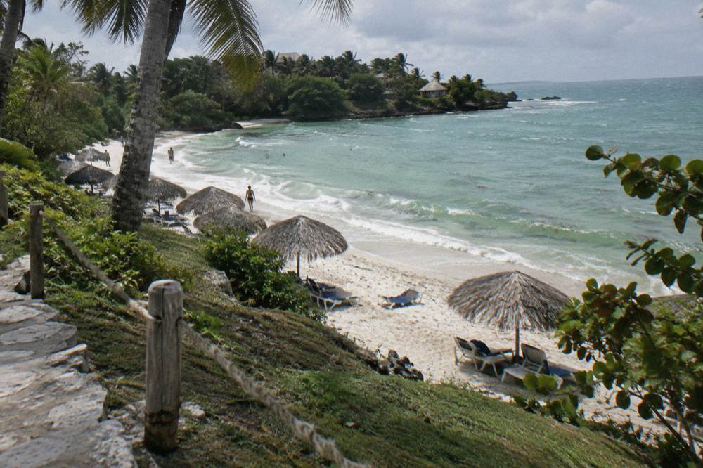 Sun loungers and thatched umbrellas along a curve of white sand with calm green water beyond