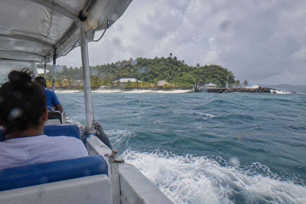 A covered tour boat crossing open bay water toward a green island