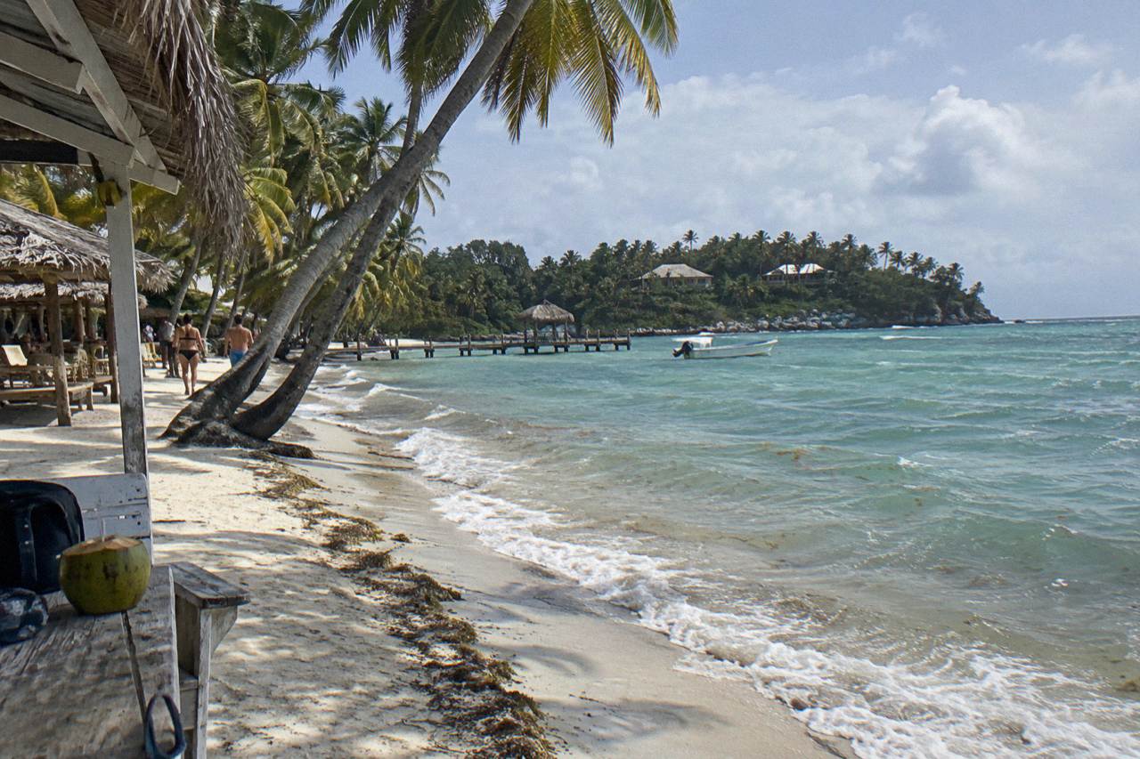 Turquoise shallow water along a palm-lined white sand beach on a small island in Samana Bay