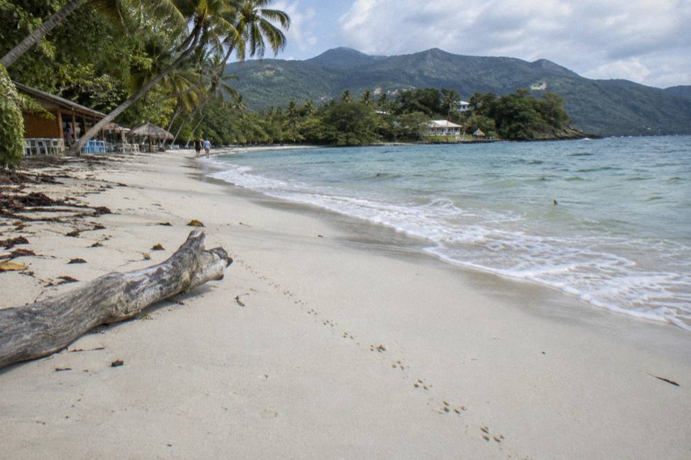 Empty white sand beach with palms and green hills behind it at morning light