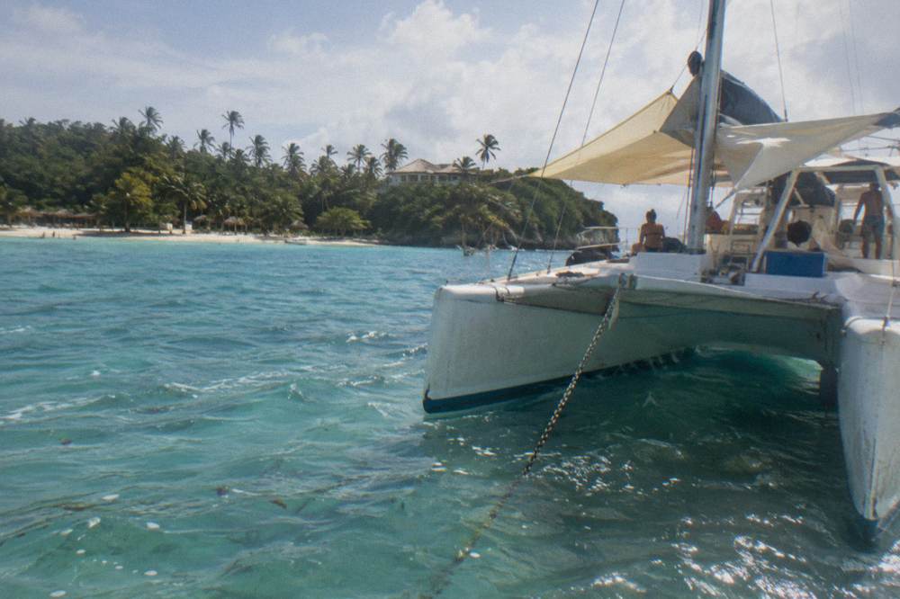 Catamaran anchored in clear shallow water near a tree lined island shore