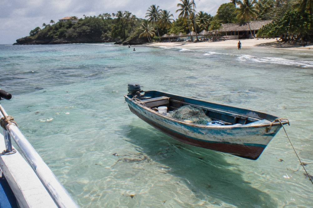 Wooden fishing boat anchored in clear shallow water near an island shoreline