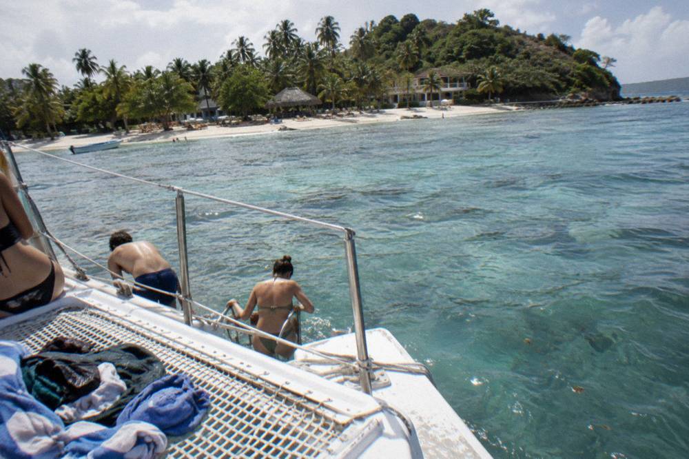 A catamaran anchored near a small tropical island with guests preparing to swim