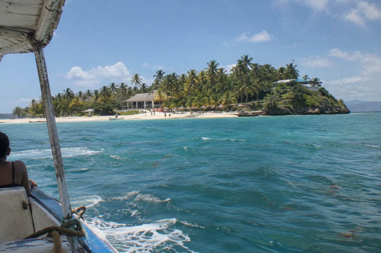 Turquoise bay water and a small palm covered island under a bright sky in Samana Bay