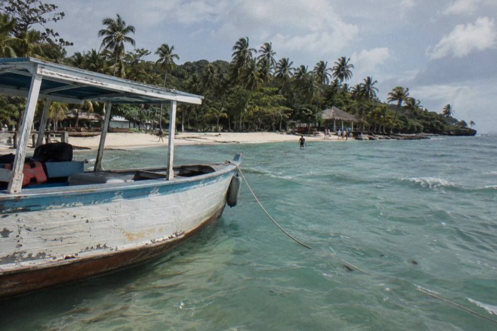 Wooden boat anchored in clear shallow water beside a palm-fringed beach
