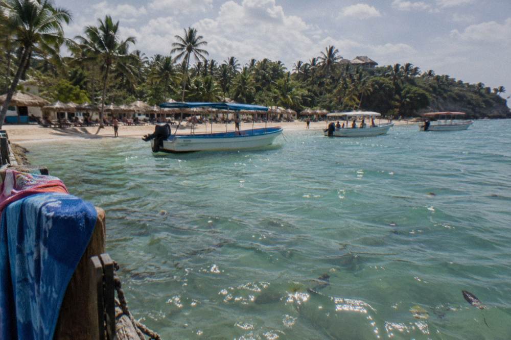 Tour boats resting in shallow water near a beach dotted with thatched umbrellas