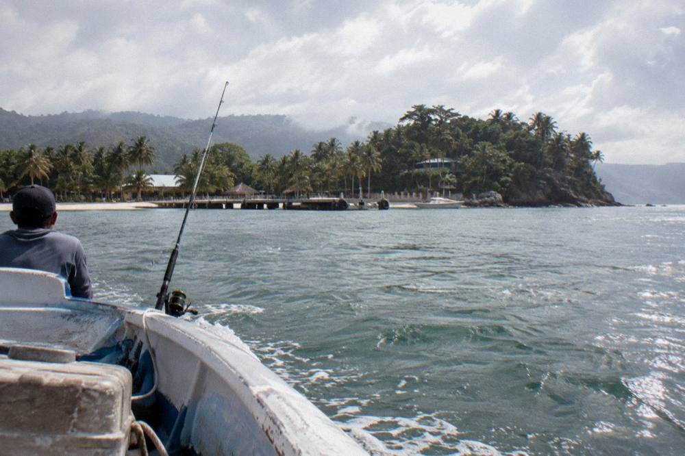 Small open boat crossing calm green water toward a tree covered island