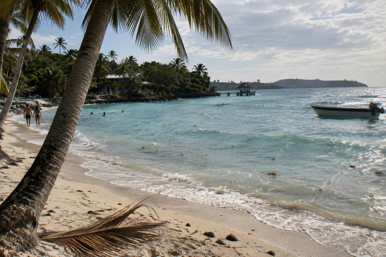 Palm trees leaning over white sand and calm turquoise water on a small Caribbean island