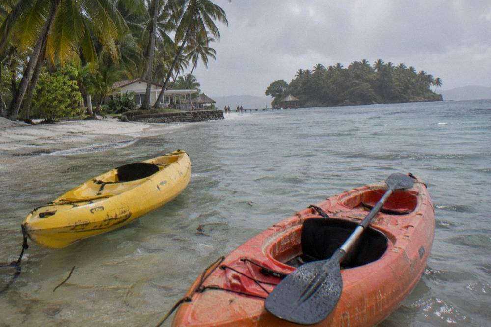 Two kayaks floating over clear shallow water beside a white sand beach lined with palms