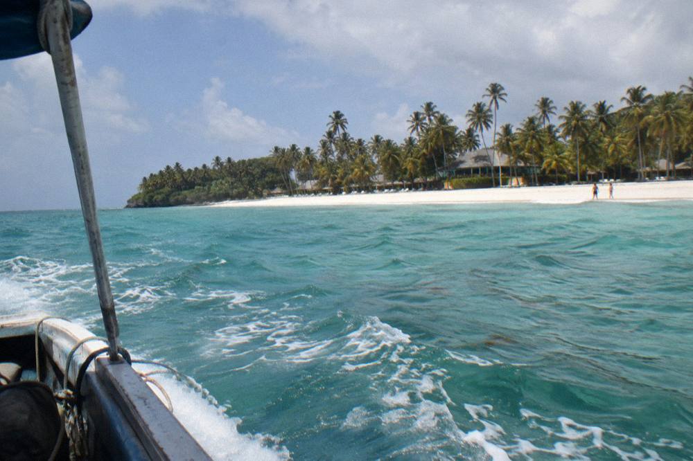 A wide sandy beach with calm turquoise shallows and a line of coconut palms along the shore