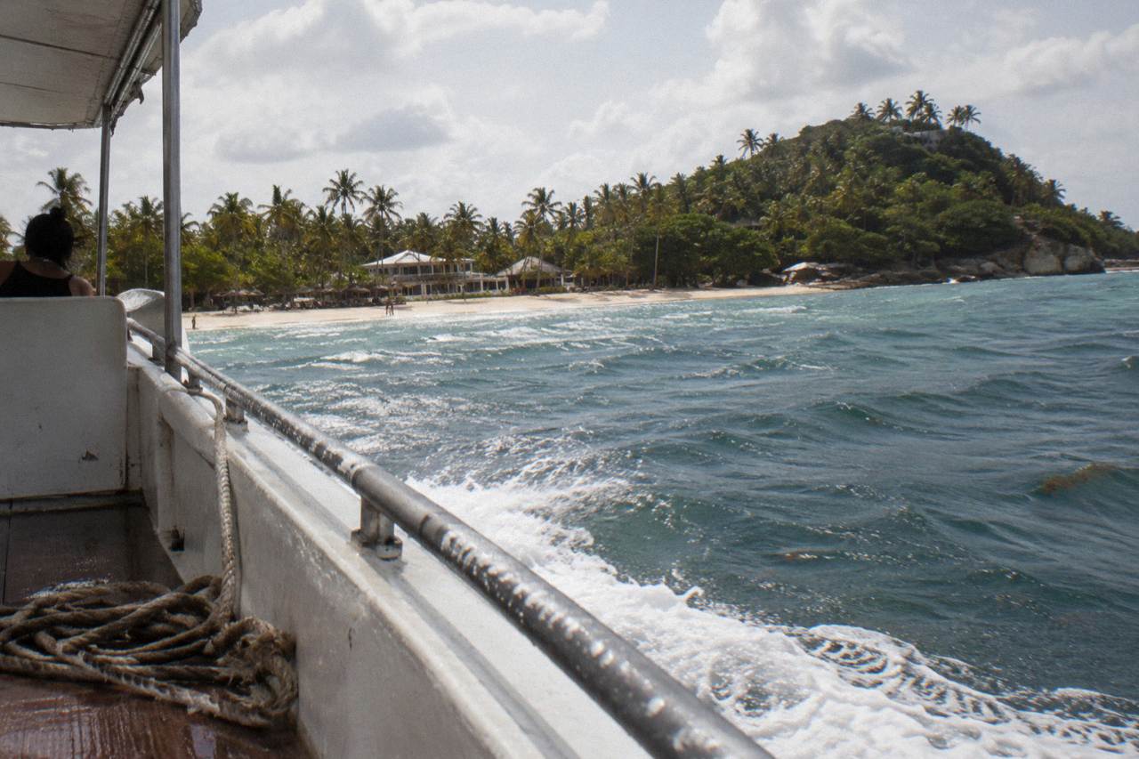 A small tour boat crossing calm turquoise water toward a palm covered island in Samana Bay