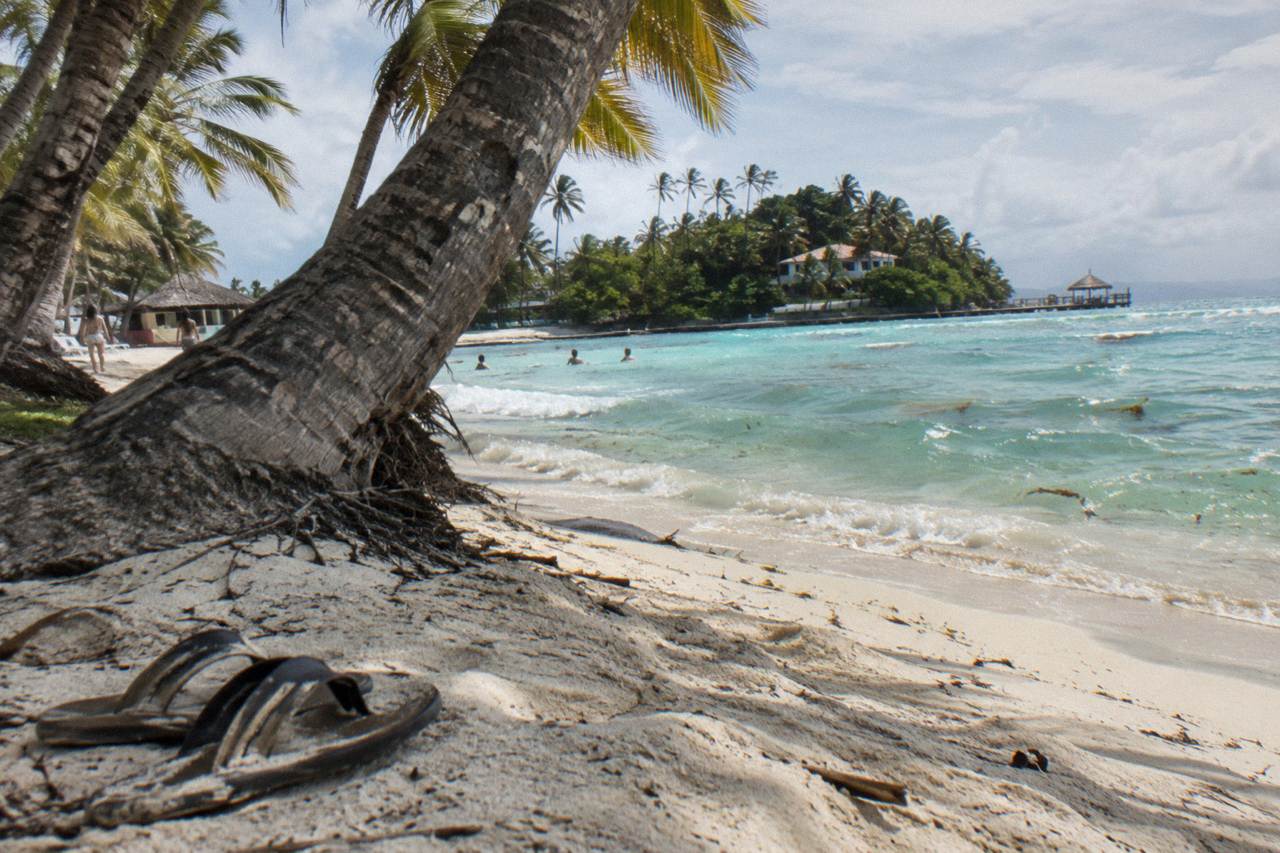 Palm trees leaning over white sand beside calm turquoise water on a small island beach