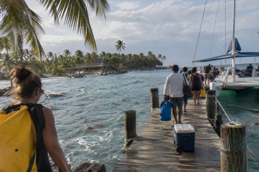 A tour bus parked beside a dock where passengers board a catamaran in the morning