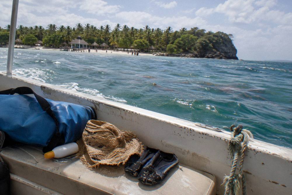 A dry bag, sunscreen, hat and water shoes arranged on a boat bench