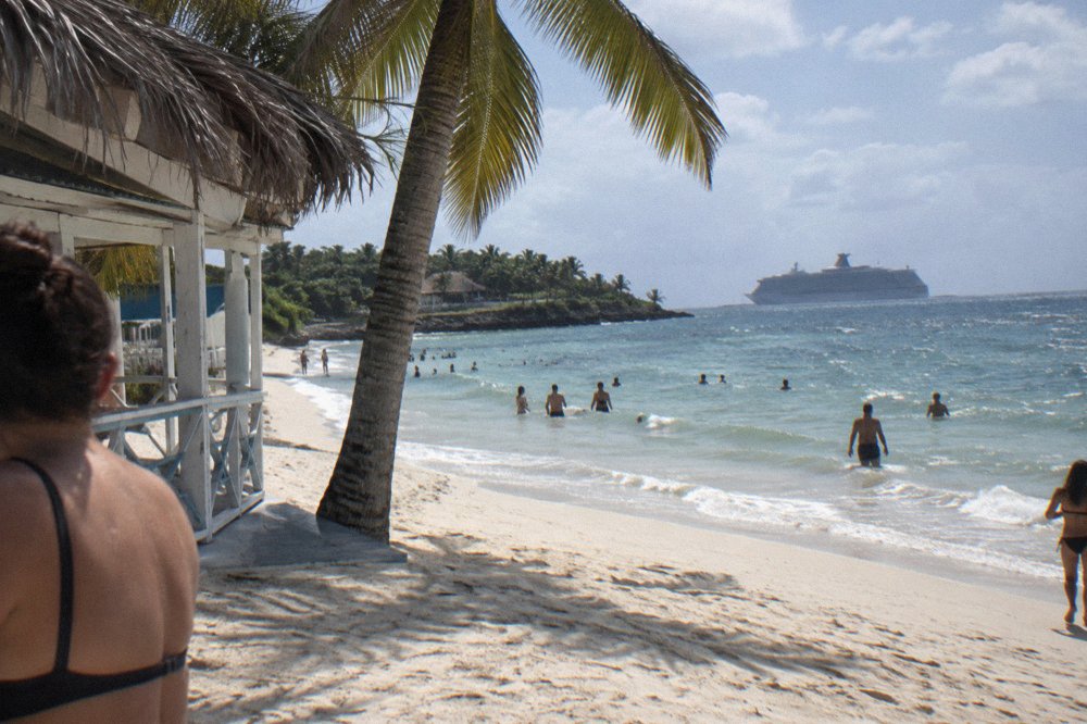 White sand beach on Cayo Levantado with a cruise ship anchored in the distance across blue bay water