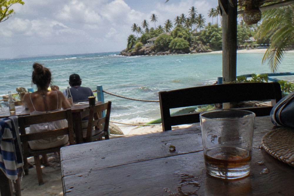 Travelers eating lunch at a shaded table overlooking turquoise bay water