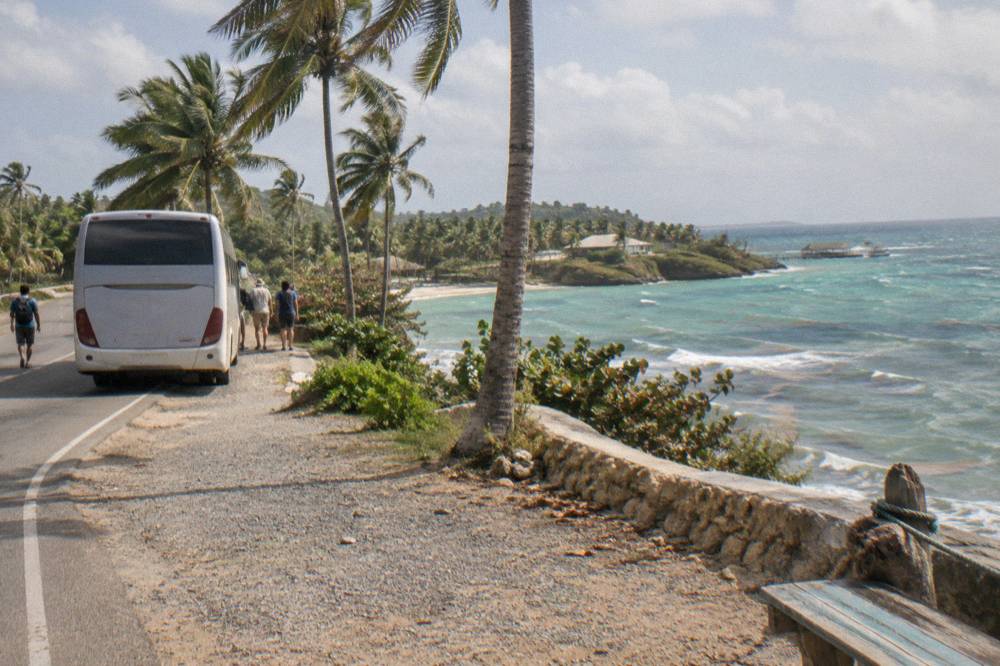 Tour bus parked on a coastal road with green hills above a bay