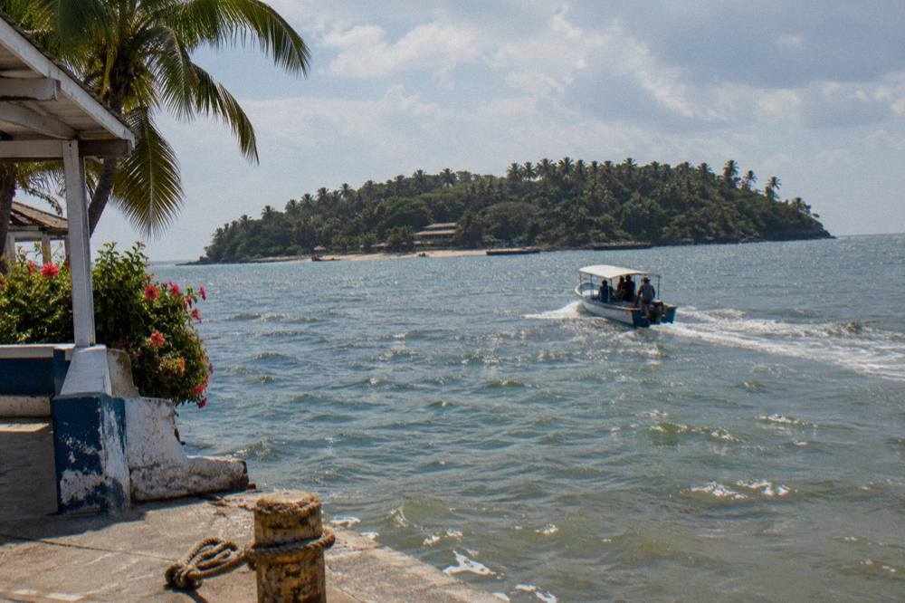 Small boat approaching a palm covered island across calm blue bay water