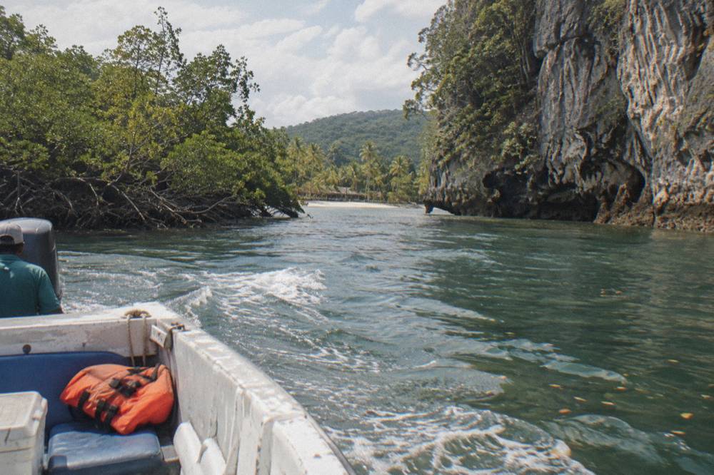 A motorboat cruising through mangrove channels beside limestone cliffs