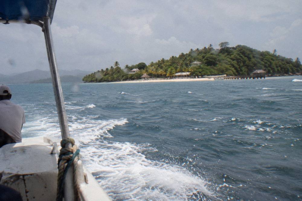 Small wooded island seen across calm blue bay water from a departing boat