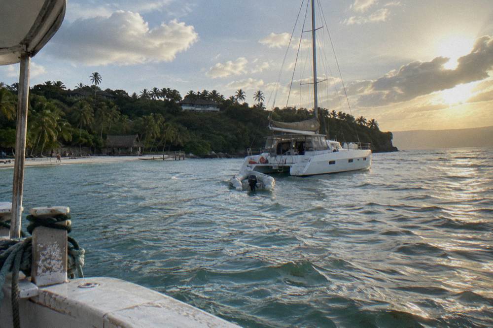 A catamaran anchored off a small green island in a wide calm bay