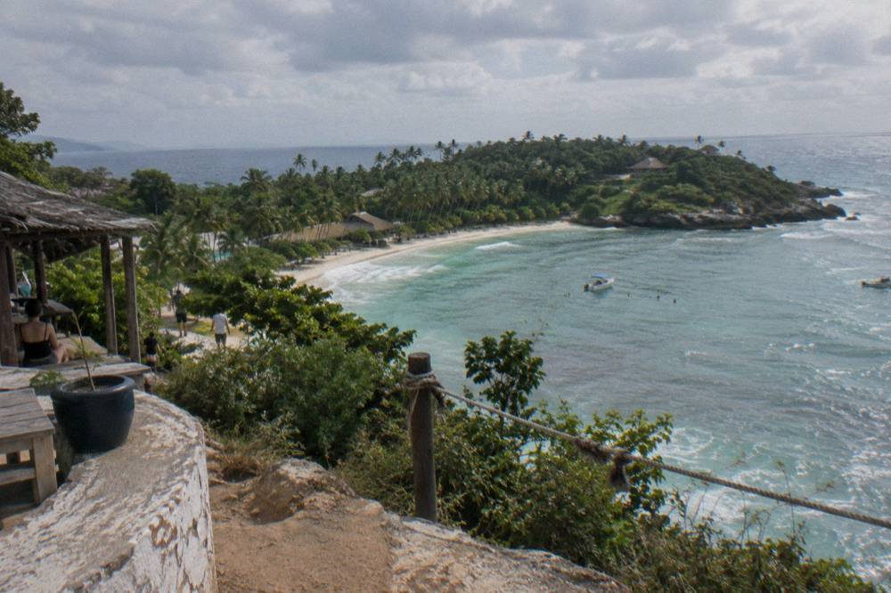 A wide view of a palm-covered island and calm bay water under scattered clouds