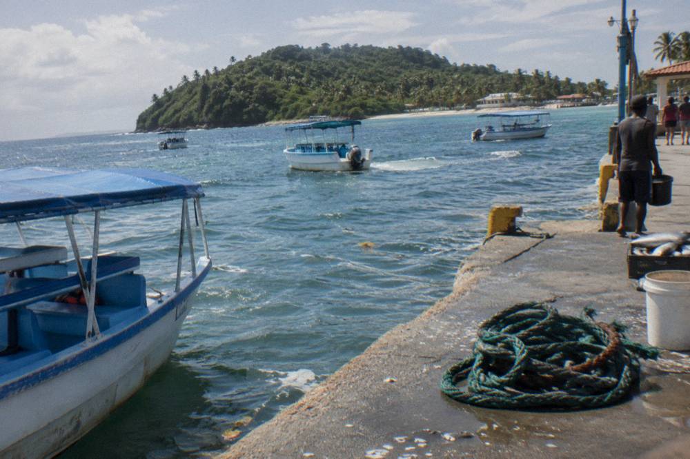 Small boats anchored in calm blue bay water near a green island shoreline