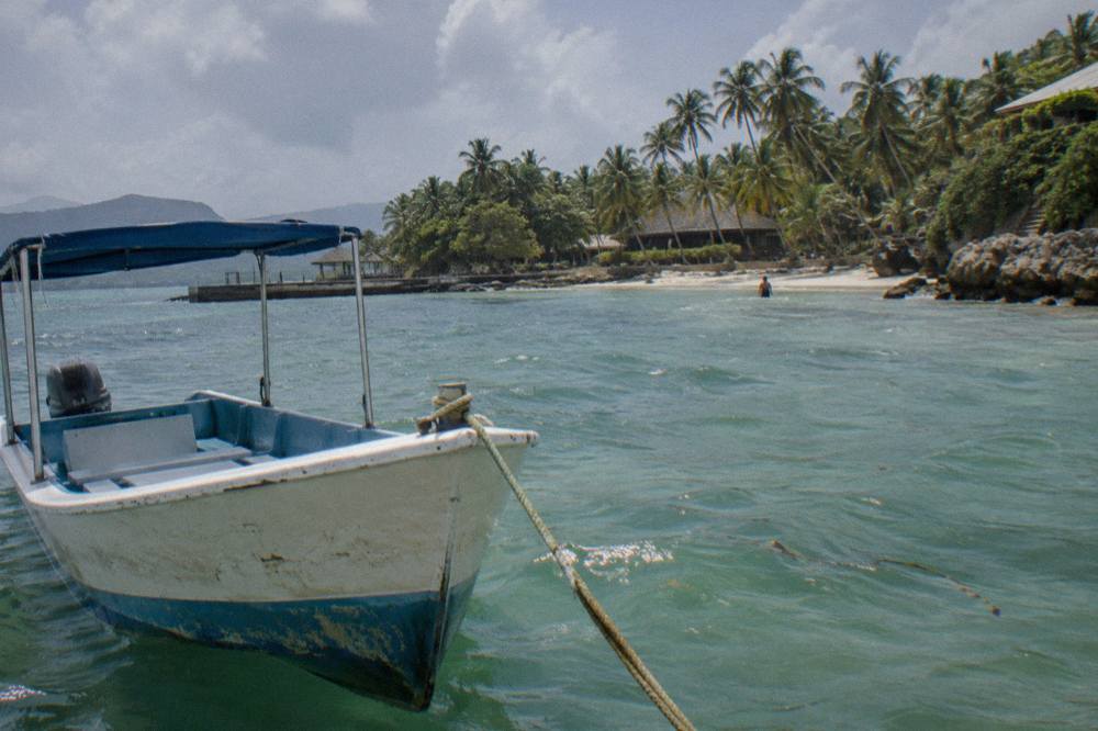 Small tour boat anchored in shallow turquoise water beside a palm-lined beach