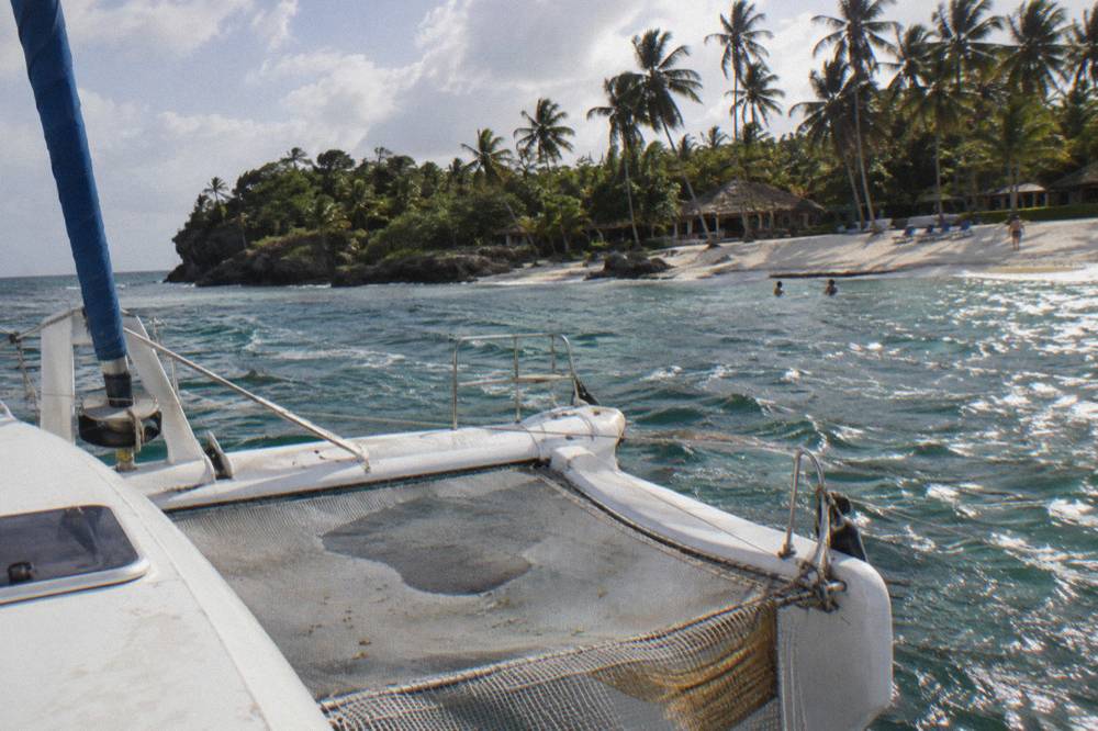Catamaran moored near a white sand beach with lounge chairs under palm trees