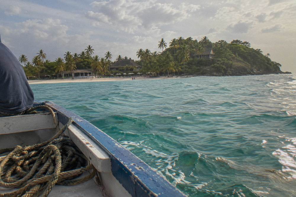 Small boat crossing calm turquoise water toward a tree-covered island