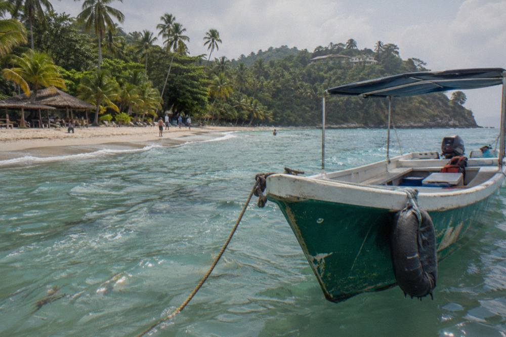 A small tour boat moored in clear shallow water beside a palm-fringed island beach