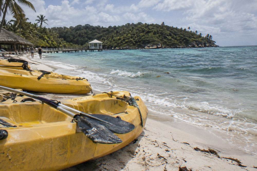 Kayaks lined up on white sand beside calm turquoise water with a forested island behind