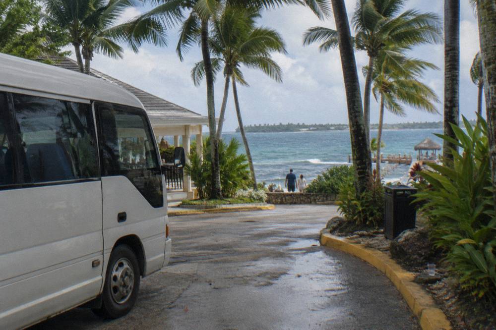 A tour minibus parked on a coastal street beside palm trees in the morning