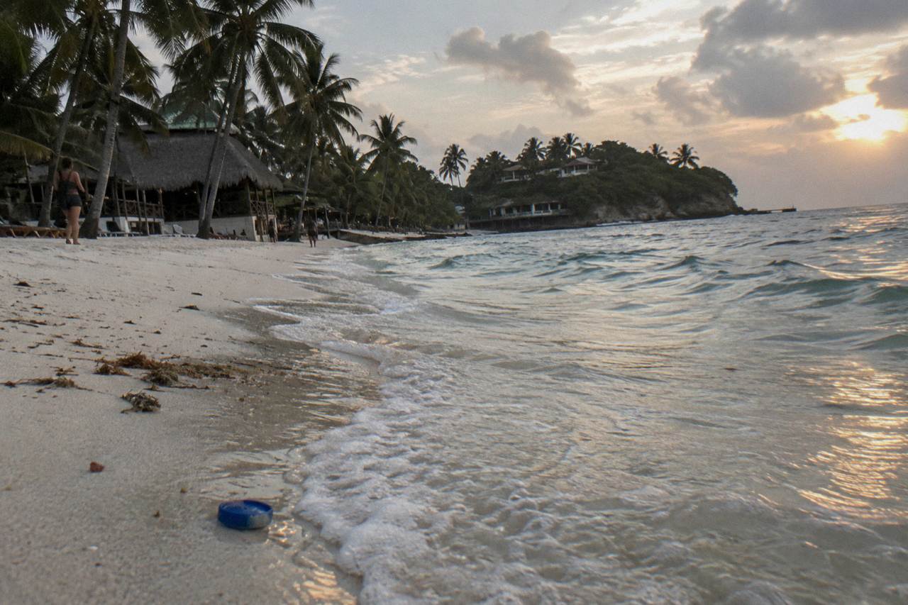 Turquoise shallow water washing onto a white sand beach lined with palm trees on a small island
