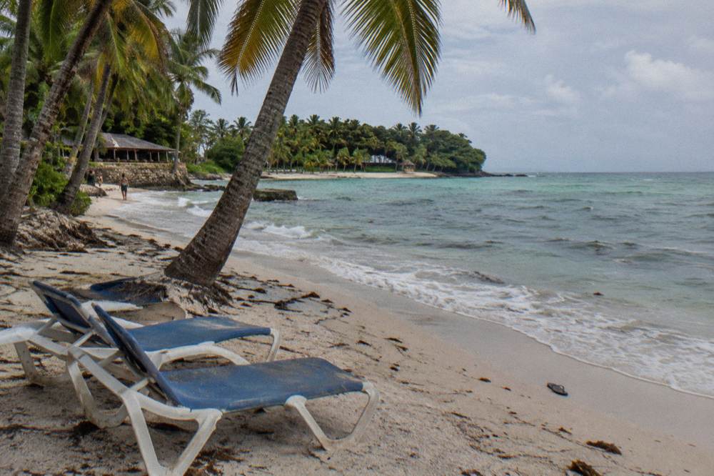 Uncrowded palm shaded beach with two empty sunloungers and gentle waves