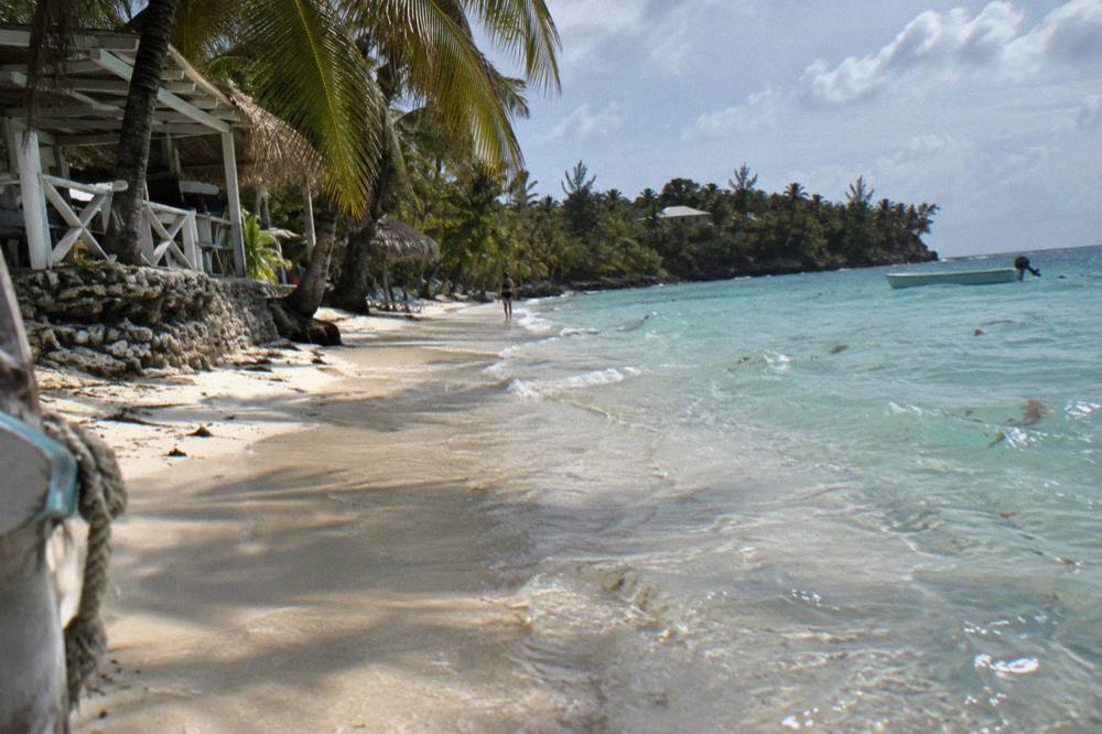 Shallow calm turquoise water over pale sand near a beach edge with palm shade