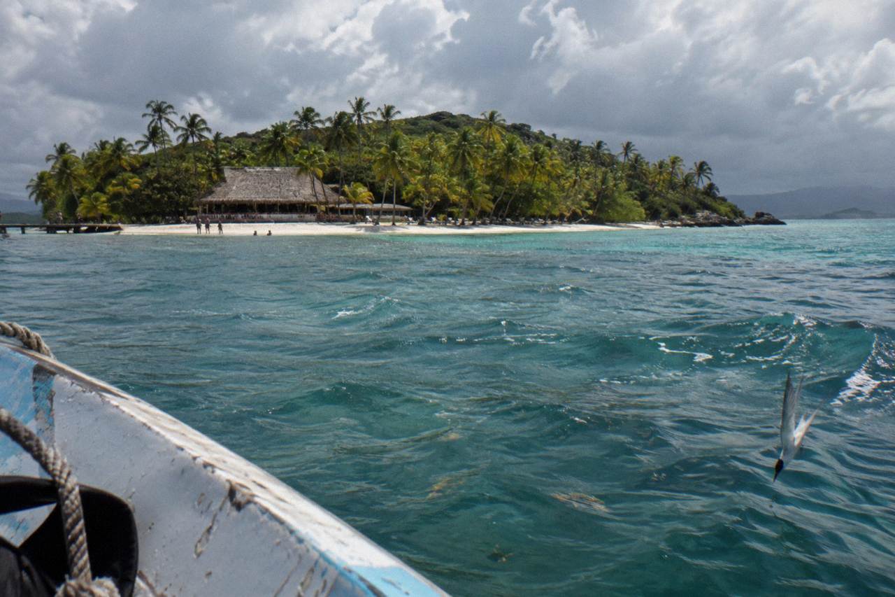 Small palm covered island with white sand beach and calm turquoise water in Samana Bay