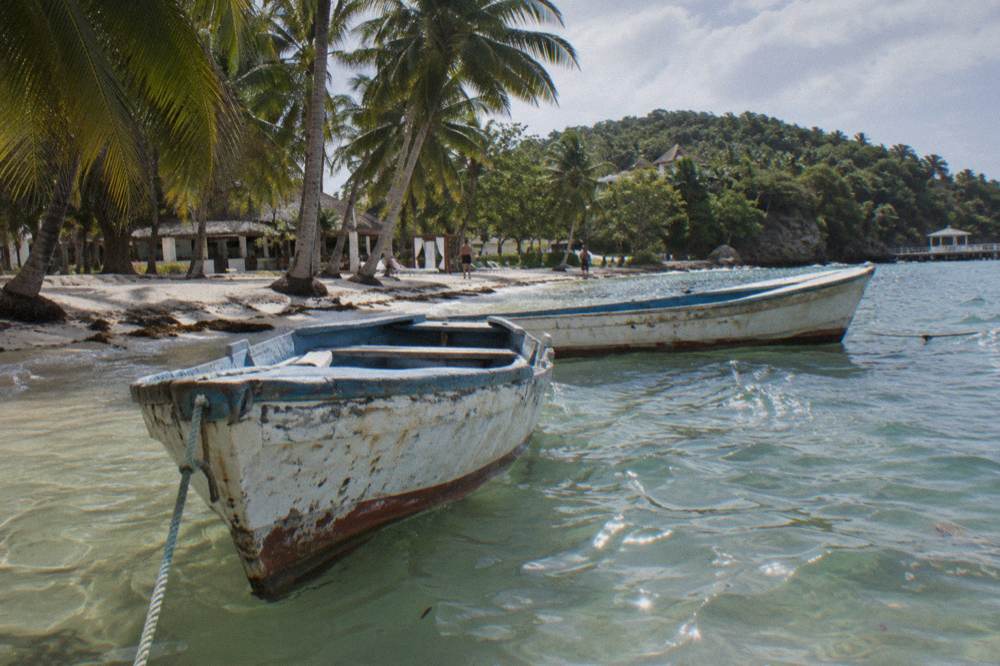 Wooden boats moored in shallow clear water beside a palm shaded island beach